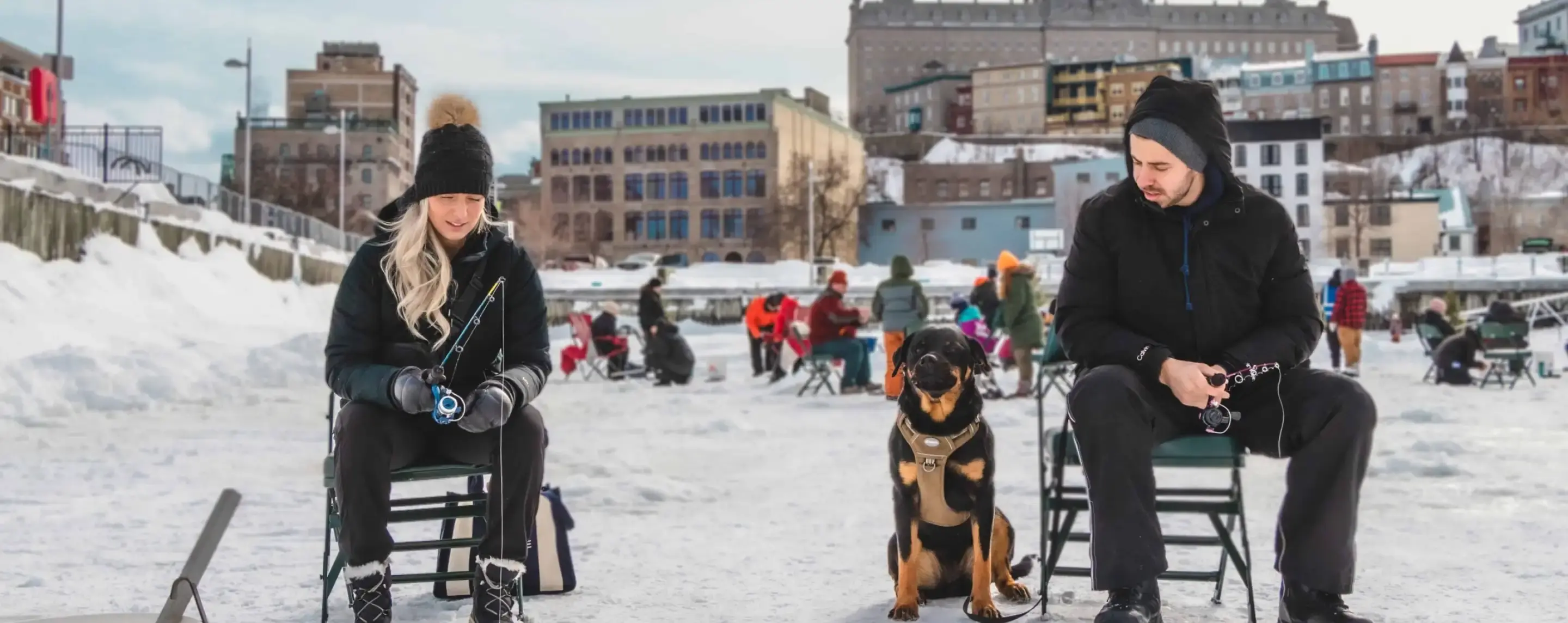 Homme et femme accompagné d'un chien qui pêche sur la glace